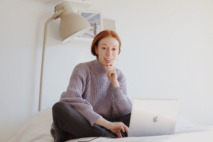 red headed woman sitting on bed with laptop