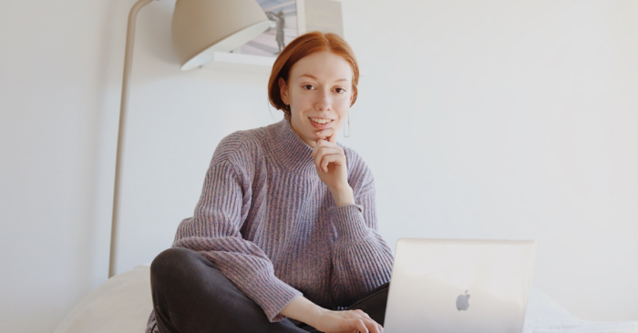 redheaded woman sitting on bed with laptop
